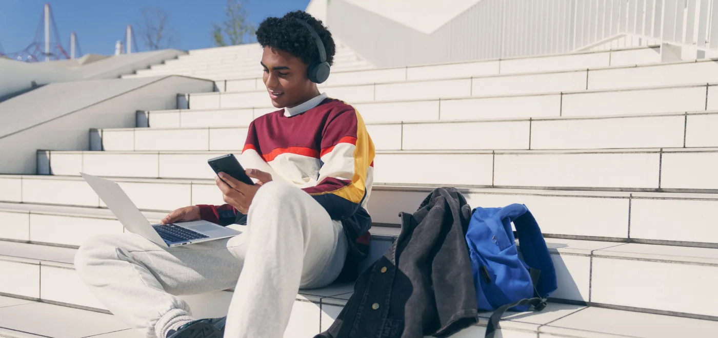 Person sitting on outdoor steps with a laptop and phone, wearing black Sony WH-CH520 headphones